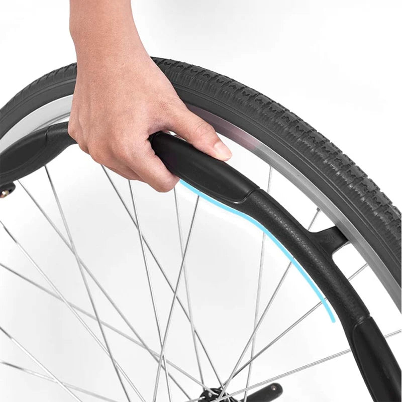A close-up view of a person's hand gripping the handrim of a wheelchair wheel. The wheel has a black tire and a metallic rim with blue reflective safety tape for visibility. The handrim appears to have an ergonomic design for a comfortable grip.