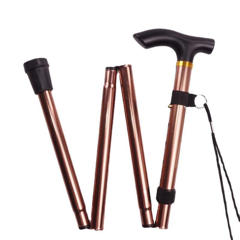 It features a stylish metallic copper finish with a comfortable black T-shaped handle and a black rubber tip for stability. The walking stick is shown in both folded and extended states, illustrating its flexibility and compact design. Additionally, there's a wrist strap attached to the handle for added security while using. This type of walking aid is ideal for individuals who need occasional support while walking, allowing them to maintain mobility and independence.